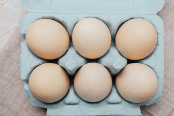 Brown chicken eggs in a blue carton box on light blue background, top view