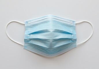 A close up shot of a light blue surgical mask with white ear loops on a white background surface view