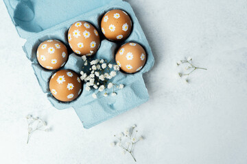 Hand-decorated Easter eggs with daisy motifs and gypsophila flowers in a blue carton. Soft spring...