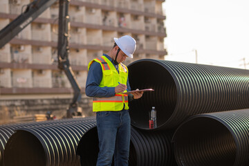 Engineer worker operations construction plans large black drainage pipe installing underground...