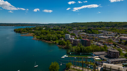 Arona,  Lake Maggiore, Italy. A vibrant aerial perspective captures a picturesque town nestled along a serene lake, with lush greenery and a brilliant blue sky.
