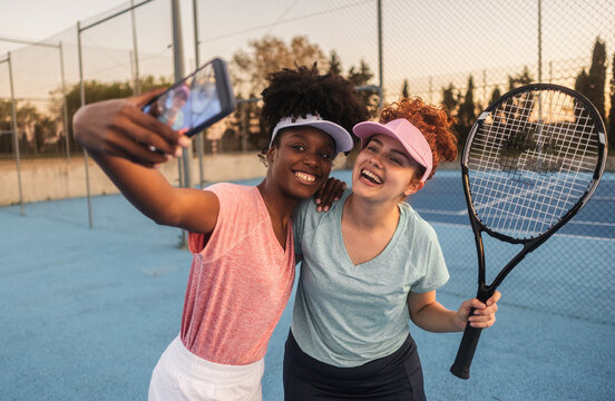 Two happy multi ethnic female tennis players taking a selfie on a paddle tennis court - Powered by Adobe