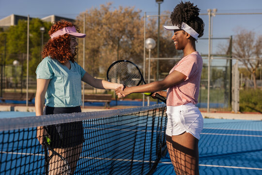 Two smiling female tennis players shaking hands over the net after match - Powered by Adobe