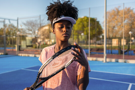 Young black woman checking tennis racket on a blue court
