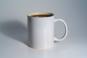 White ceramic mug filled with coffee on neutral background