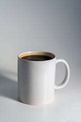 White ceramic mug filled with coffee on clean light background