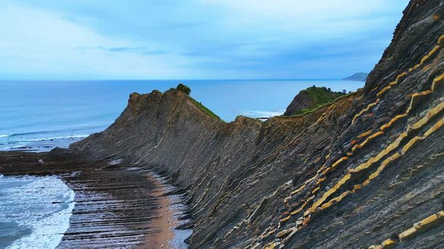 Roches en strates Flysch vue de pr&egrave;s en gros plan jusqu'aux vagues de l'oc&eacute;an, roche grise, jaune, collines et falaises. Drone 
