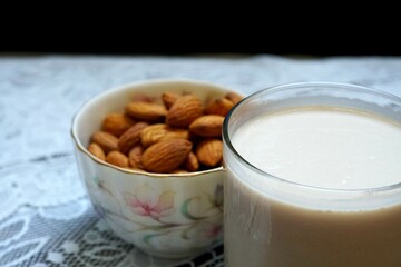 A glass of almonds milk and a cup of almonds on a table