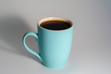 Turquoise mug filled with black coffee on light background