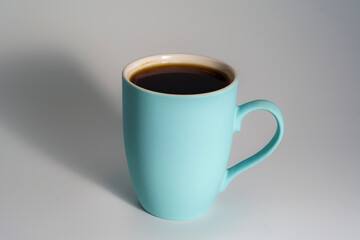 Light blue ceramic mug filled with coffee on neutral background