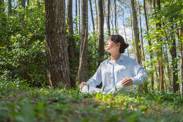 A young asian woman wearing a long-sleeve collared shirt and denim jeans pants is meditating and...