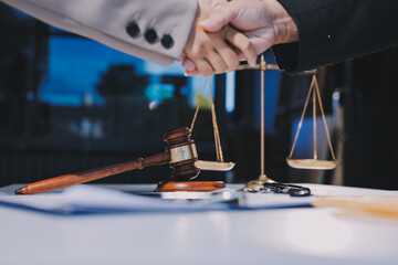 Two businesspeople are shaking hands in a law office with a scale and a gavel on the table.