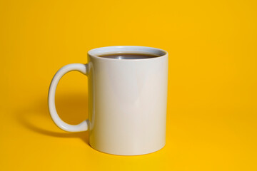 White ceramic mug filled with coffee on yellow background