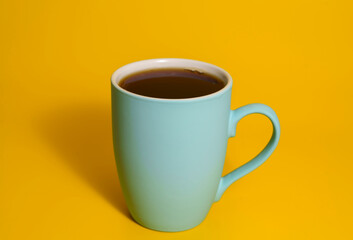 Blue coffee mug with black coffee on yellow background
