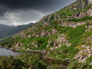 Overlooking a tranquil river, the image captures steep rocky hills blanketed in greenery. Dark...
