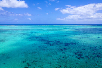 aerial view of turquoise clear tropical water and coral barrel on blue cloudy sky background, Mauritius island
