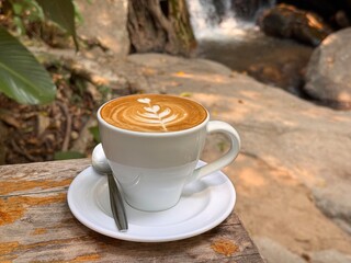 Steaming Café Latte with Breathtaking Waterfall Forest View Background