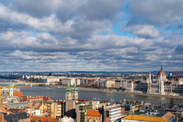 Obraz premium Panoramic view of Budapest with the Hungarian Parliament Building and Danube River under a dramatic sky.