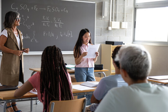Smiling student presenting work in chemistry class with teacher and students watching