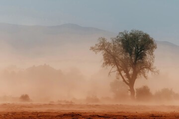 Fototapeta premium A dramatic scene of a lone dry tree standing amidst a swirling dusty desert storm, fine red dust filling the air and partially obscuring the background, faint silhouettes of distant hills 