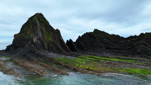 Vol lat&eacute;ral face &agrave; l'&icirc;le de roche noire stri&eacute;e - Contrastes noir et vert &agrave; Saturraran Ondartza (16:9)