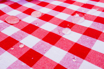 Raindrops on red checkered tablecloth with white squares close up pattern