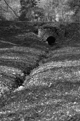 Monochrome concept with a stream flowing diagonally in a ravine and a dark drainage hole made of old brickwork