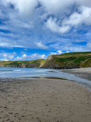 Scenic coastal landscape with sandy beach and cliffs under a cloudy blue sky – original photo by contributor
