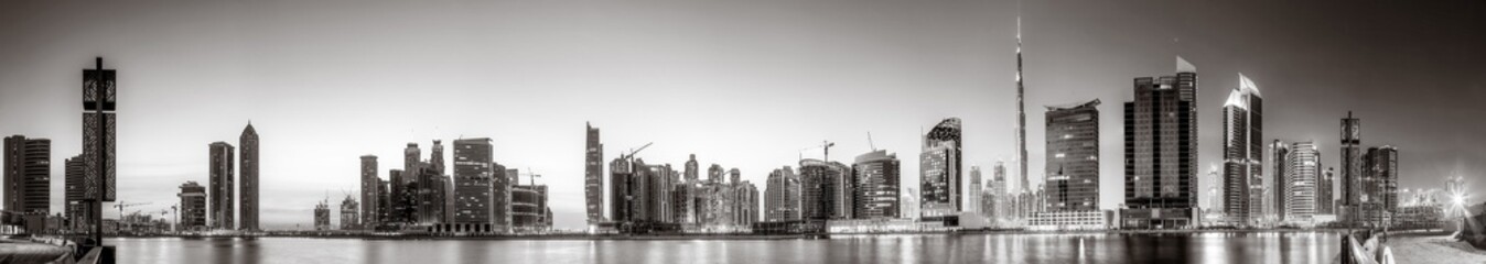 Fototapeta premium Monochrome city skyline with tall skyscrapers reflecting on calm water under a cloudy sky, Dubai Marina bay UAE