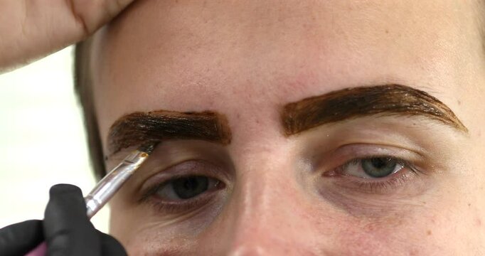 A beautician does henna eyebrow tinting for the young woman, cosmetological procedures and beautycare