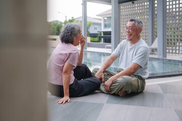 Fototapeta premium Asian Elderly couple sitting on floor by pool, sharing joyful moment and laughing together. scene captures sense of happiness and companionship in serene outdoor setting