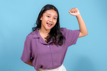 Happy young Asian woman smiling brightly with an enthusiastic expression, raising her fist in...