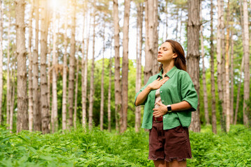 Young adult woman in green shirt practising breathing exercise in the forest.