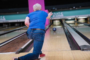 Senior man throwing bowling ball down the lane, aiming for a strike in a bowling alley, showing his skill and precision in the game