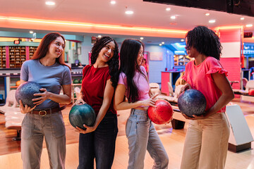 Four friends are holding bowling balls and chatting together, enjoying their leisure time at the...