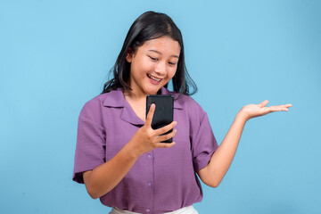 Smiling young Asian woman looking at smartphone while raising her palm to present something. Her...