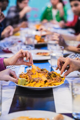 Hands grabbing nachos with melted cheese, guacamole and jalapenos from a plate in a restaurant