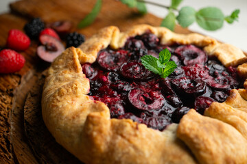 Galette tart with red berries, cherries, raspberries and blackberries. Top view table with christmas decoration.