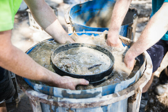 Hands in muddy water of fossicking drum holding sieve