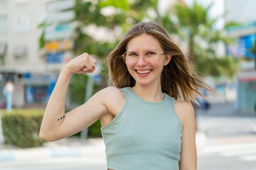 Young blonde woman with glasses at outdoors doing strong gesture