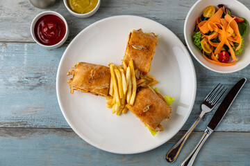 Healthy chicken sandwich served on a white porcelain plate with french fries and sauces