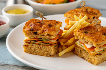 Square gourmet sandwiches with fries served on a white plate