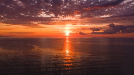 Fototapeta premium Vibrant Sunset Over Ocean With Light Beam and Distant Silhouette