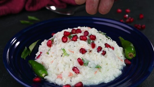 Curd rice served in a plate and garnished with pomegrante seeds.