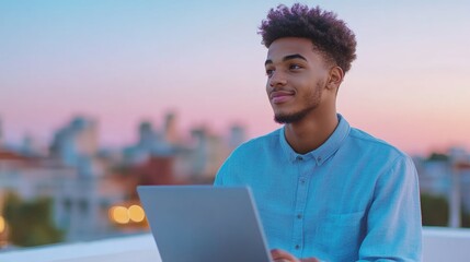 Young man using laptop on rooftop at sunset, contemplating future opportunities.