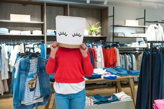 Cheerful young woman wearing a paper bag on her head shopping for fashion in a mall highlighting fun and great clothing sales