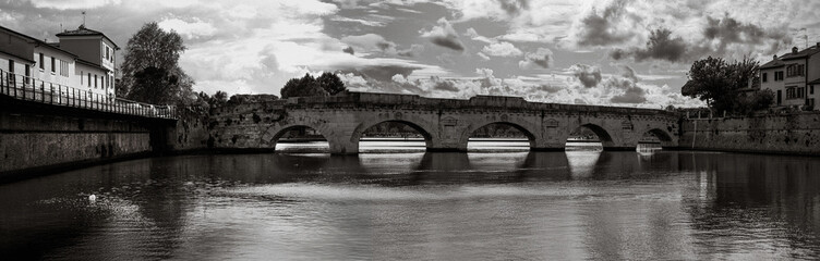 Fototapeta premium Rimini city skyline over the historic bridge Ponte di Tiberio and the Marecchia River in the Emilia-Romagna region of Italy, captured in a tranquil black and white retro-style panoramic photo