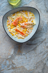 Bowl of crab and corn chowder, vertical shot on a blue and beige stone background, copy space, above view