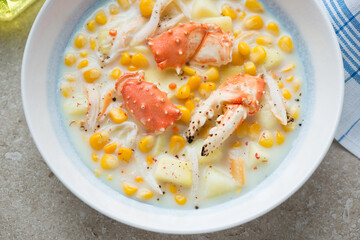 Corn chowder with crab meat served in a white and blue plate, horizontal shot, middle close-up, selective focus