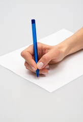 Hand holding a blue pen writing on white paper